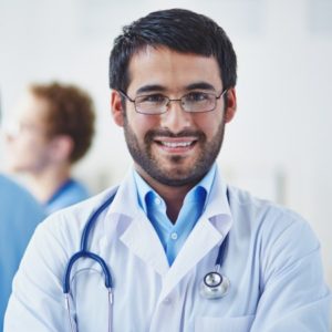 Portrait of smiling doctor looking at camera on background of his working colleagues